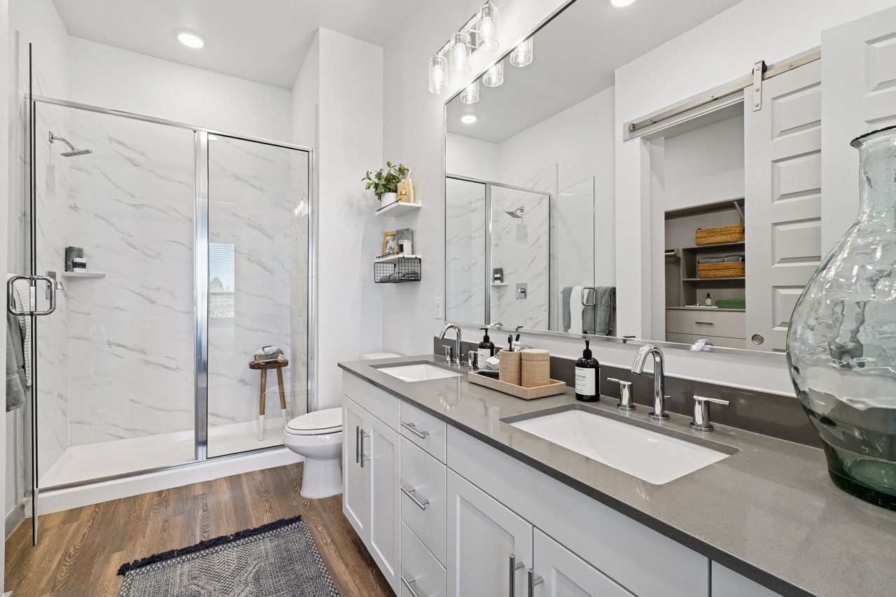 Modern bathroom with dual sinks, glass-enclosed shower, white cabinets, and a large mirror  at Ennova Fulshear in Fulshear, TX.