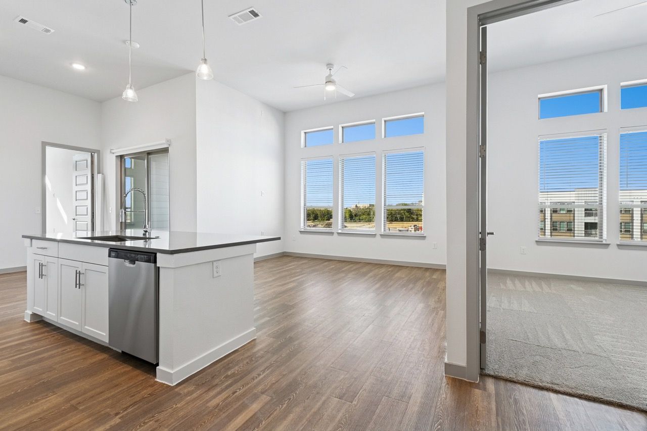 Open-concept kitchen with island, sink, stainless dishwasher, and large windows in a bright living area  at Ennova Fulshear in Fulshear, TX.