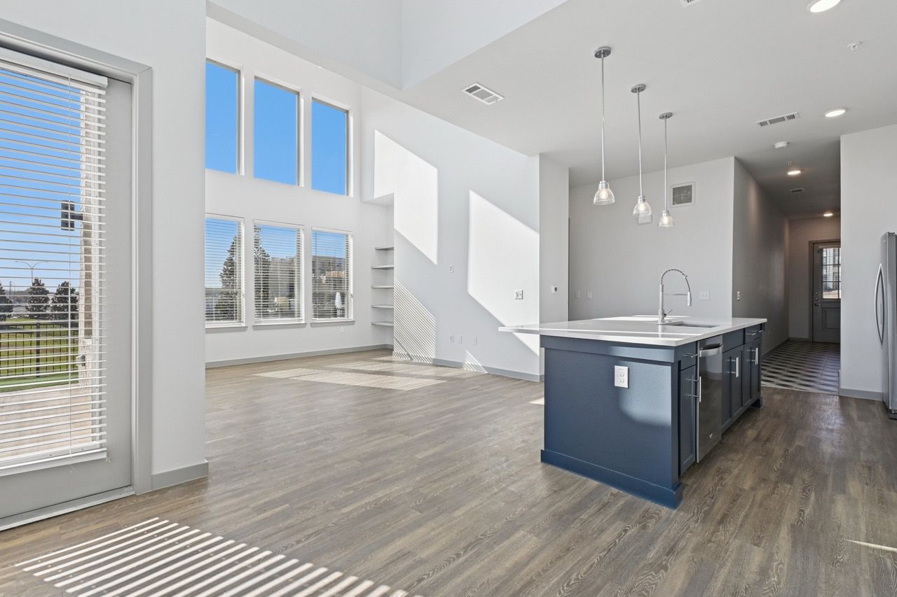Open-concept kitchen with blue island, pendant lights, and large windows  at Ennova Fulshear in Fulshear, TX.
