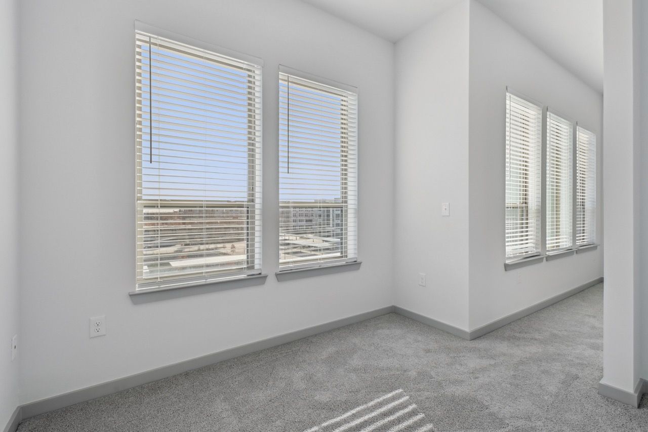 Bright empty apartment room with large windows and white blinds  at Ennova Fulshear in Fulshear, TX.