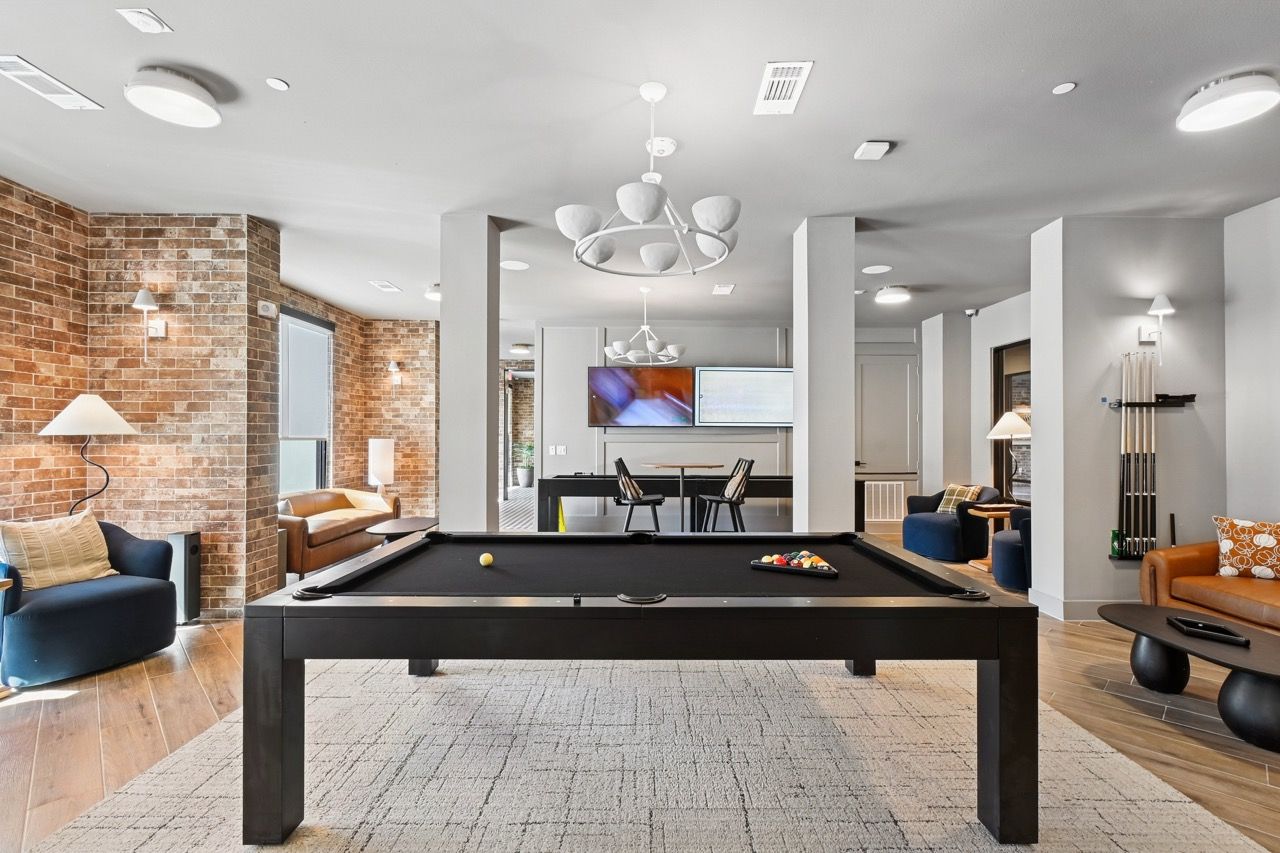 Interior community lounge with a billiards table, seating, and wall-mounted TVs at Ennova Fulshear in Fulshear, TX.