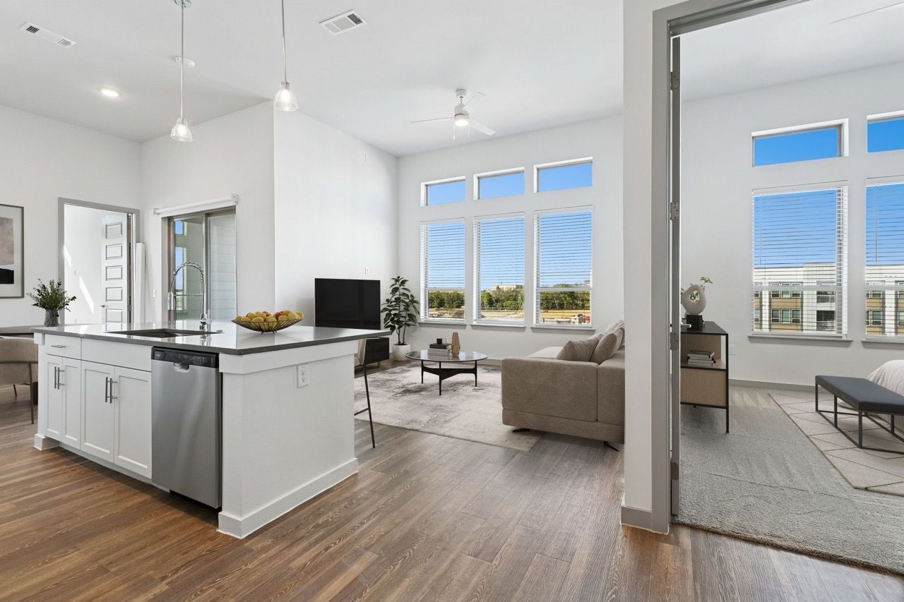 Open-concept kitchen and living room with island, hardwood floors, and large windows  at Ennova Fulshear in Fulshear, TX.