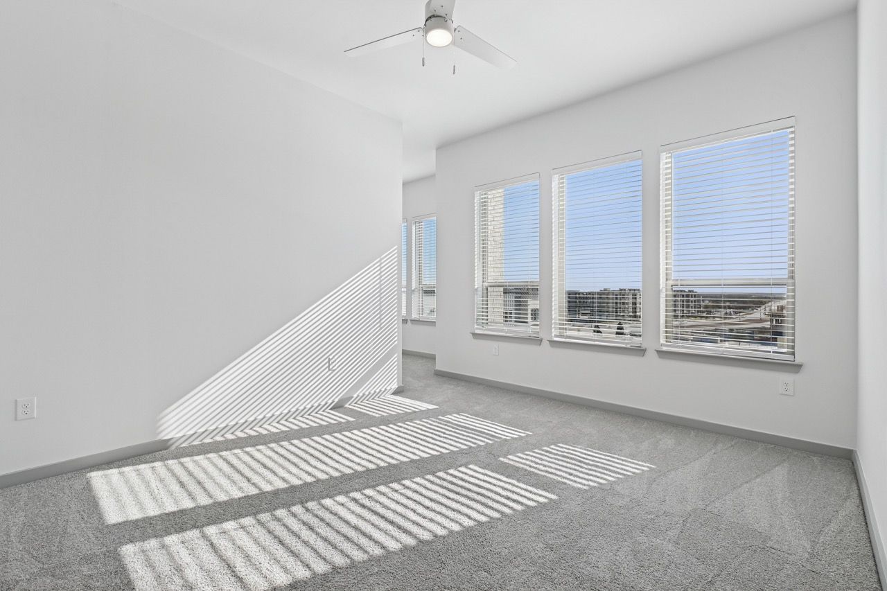 Bright empty apartment room with multiple windows and a ceiling fan  at Ennova Fulshear in Fulshear, TX.