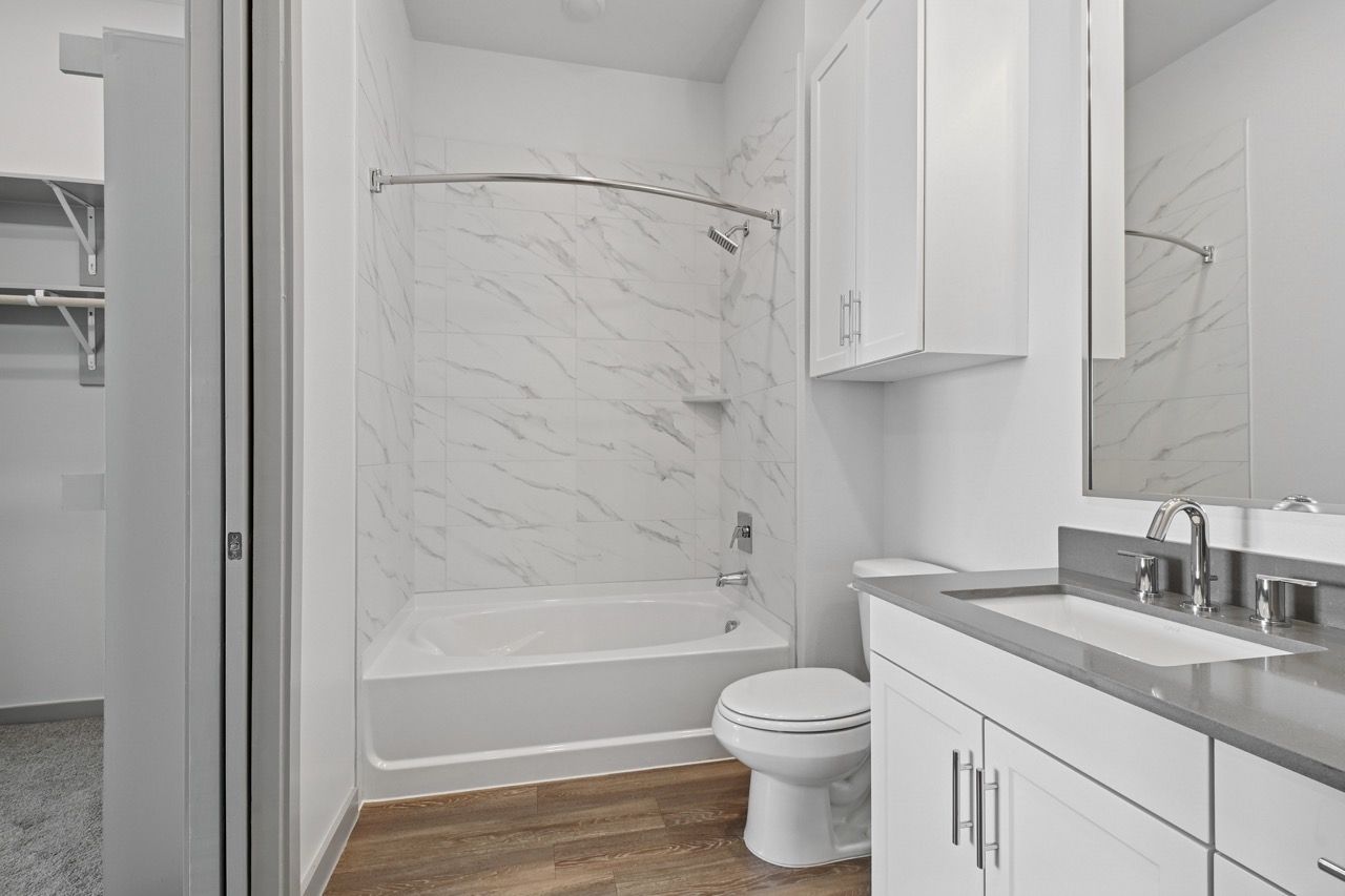 White bathroom with tub/shower, toilet, and vanity  at Ennova Fulshear in Fulshear, TX.