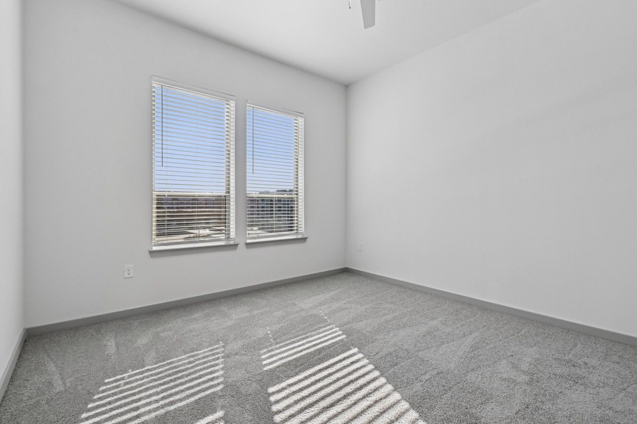 Empty bedroom in a modern apartment with two windows and blinds  at Ennova Fulshear in Fulshear, TX.