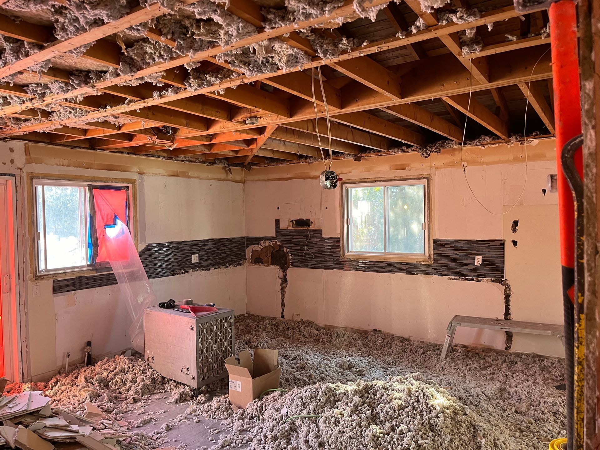 Intérieur d'une cuisine en rénovation, avec poutres apparentes au plafond, isolation au sol et dosseret partiel en carrelage.