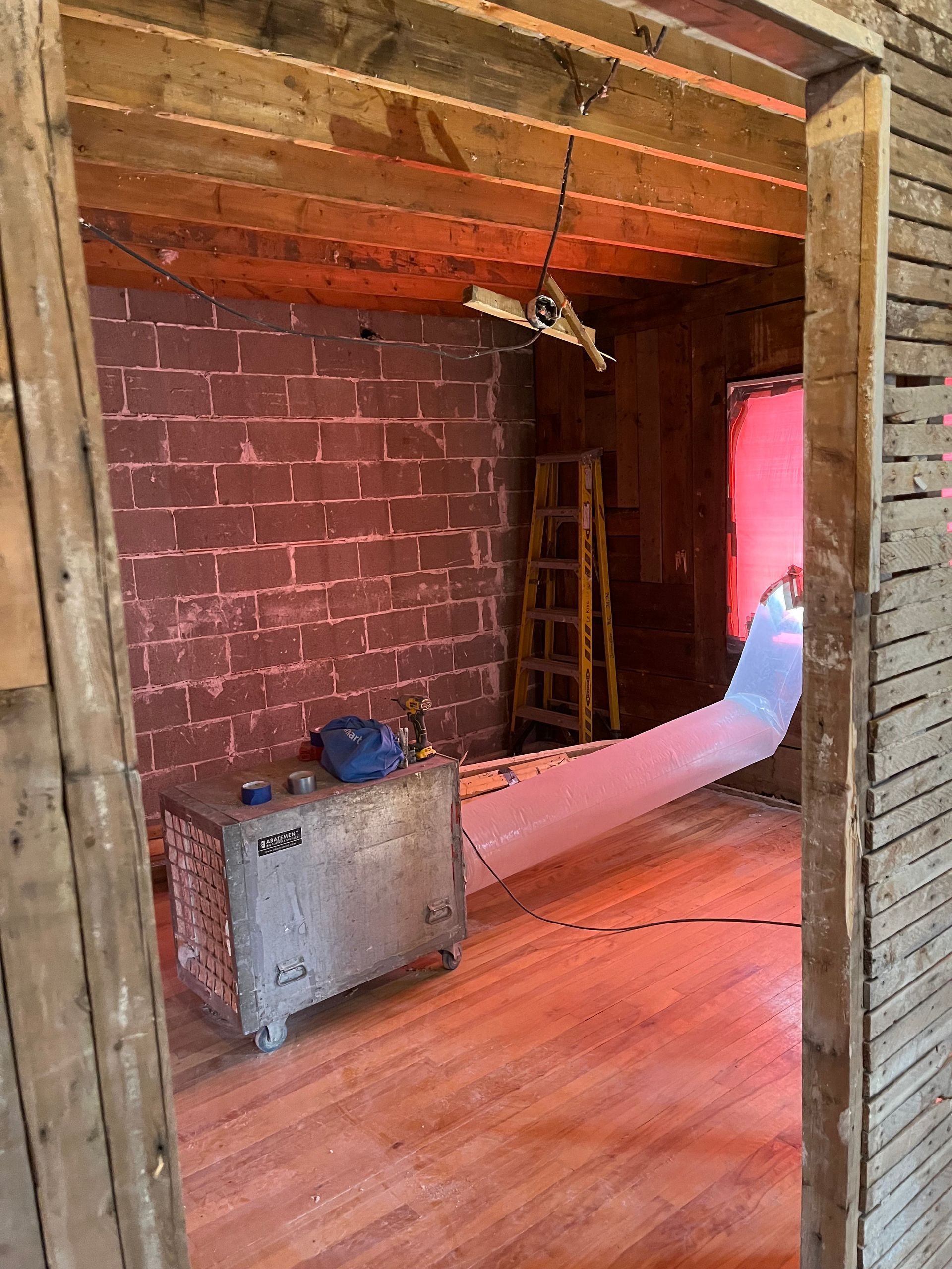 Chambre en construction avec murs en briques apparentes et poutres en bois, dotée d'un radiateur et d'un tube de ventilation.