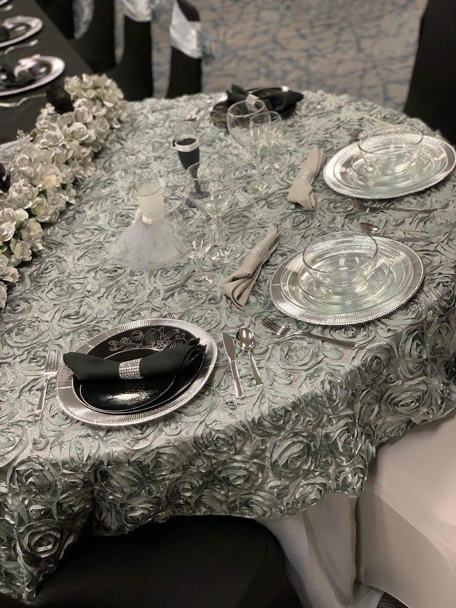 Elegant table setting with silver chargers, black plates, folded napkins, and a patterned silver tablecloth