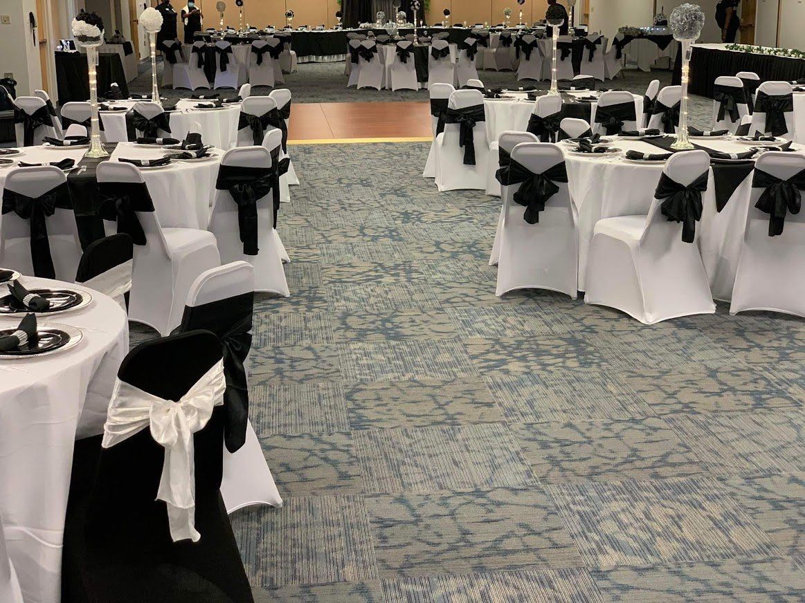Banquet hall with round tables dressed in white and black linens, set for an event.