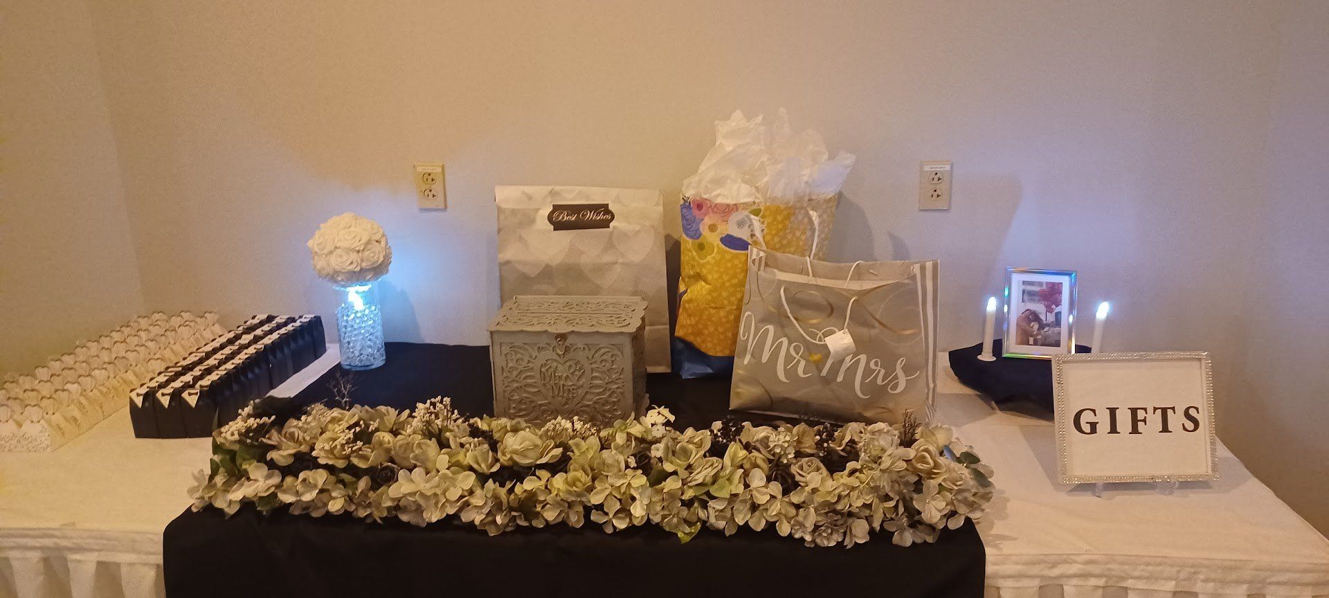 Decorated gift table with wrapped presents, a white box marked “GIFTS,” and flowers in the center