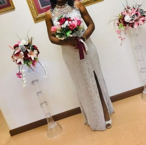 Woman in a silver gown holding a pink and white bouquet beside floral stands in a decorated room