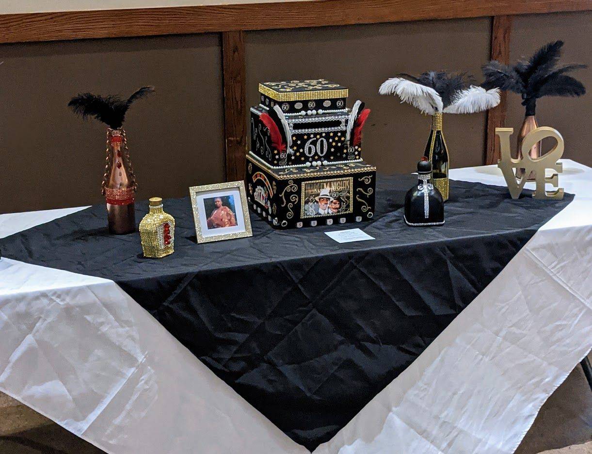 Decorated table with black-and-white cloth, gold accents, feathers, and stacked gift boxes.