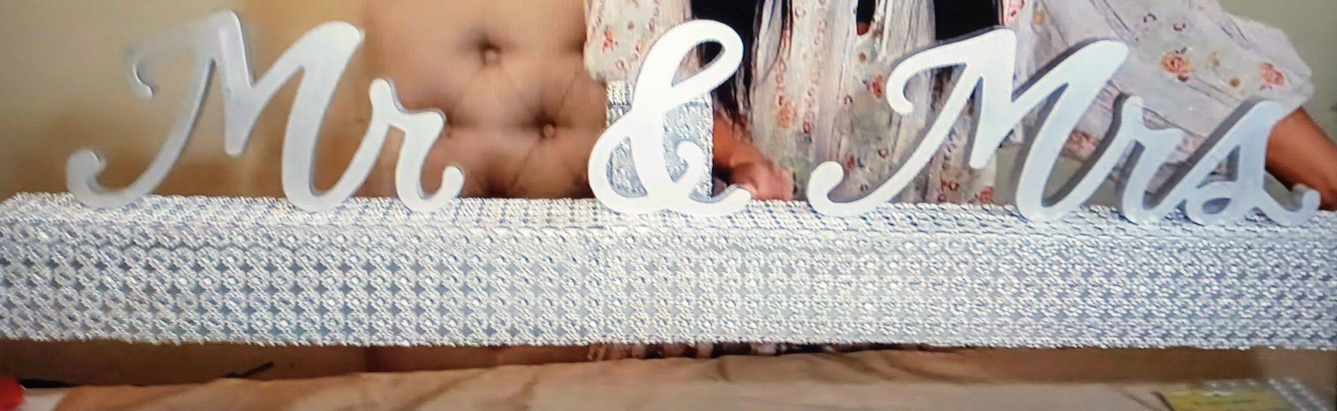White “Mr & Mrs” sign on a tufted white couch in front of a beige floral backdrop.