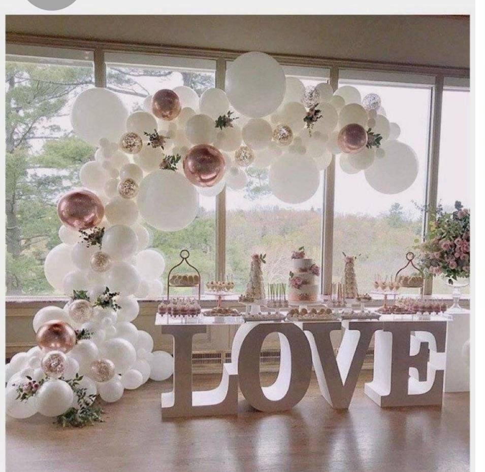 Elegant white and blush balloon arch beside a table with large LOVE letters in a bright room