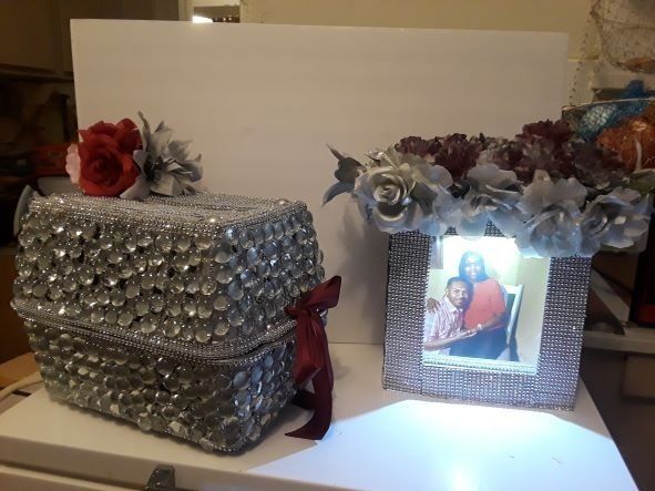 Two jeweled gift boxes with floral decorations, one showing a lit photo frame on the front.