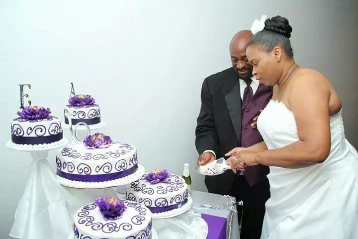 Bride and man cutting a white and purple wedding cake at a reception table