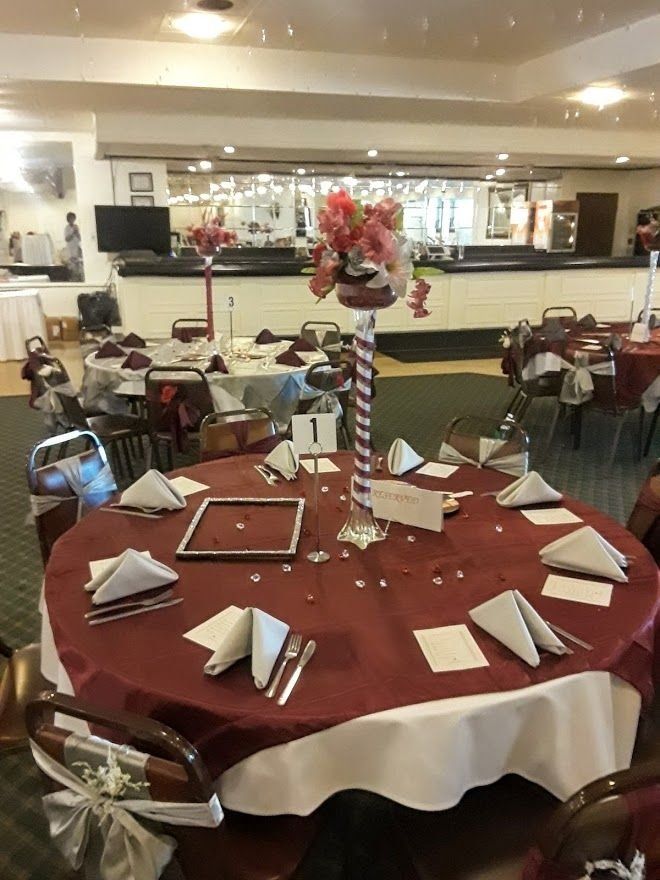 Round banquet table with red tablecloth, folded napkins, and floral centerpiece in a reception hall.