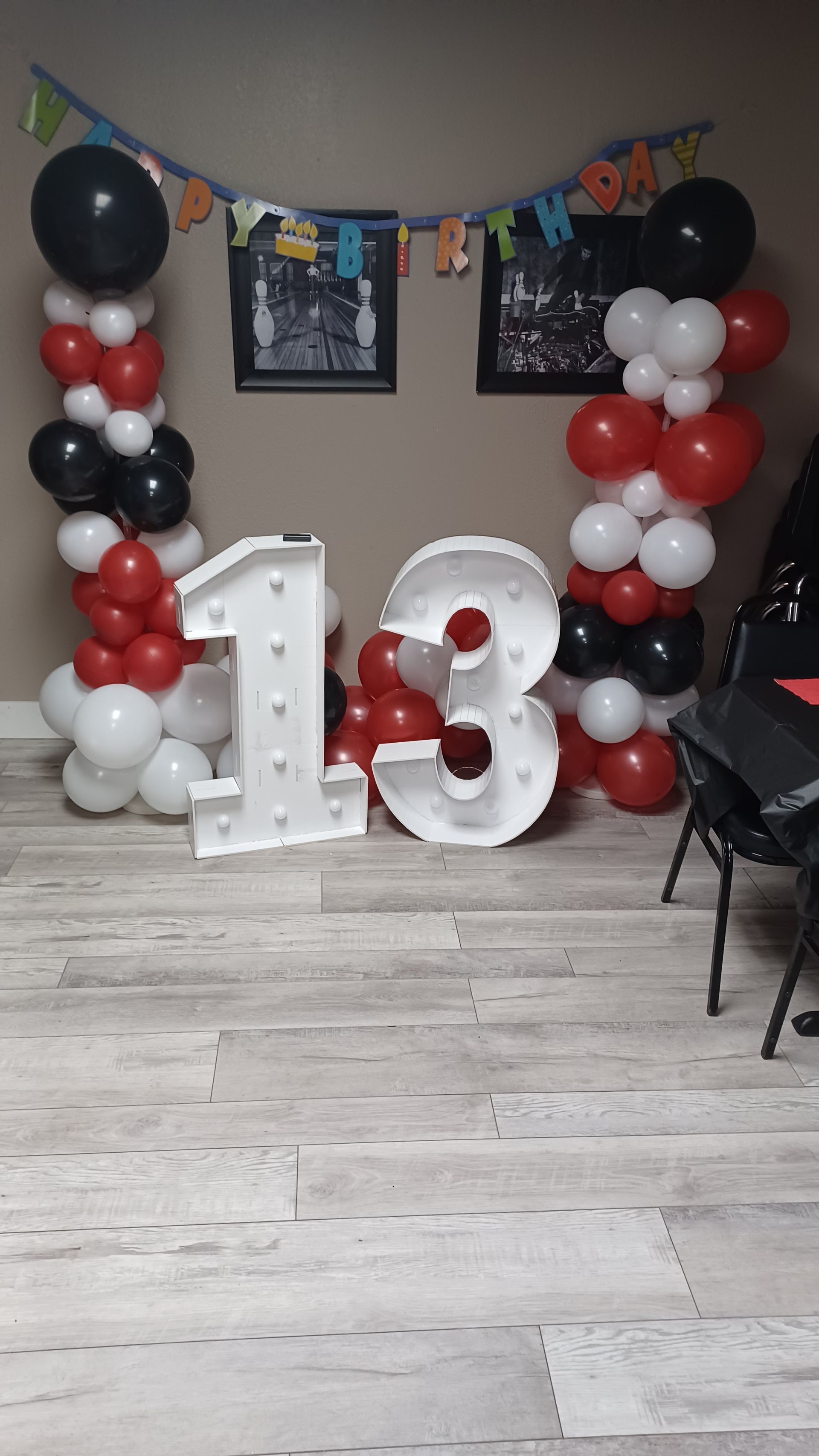 Birthday party setup with large white 13 balloons and black, red, and white balloon columns in a room