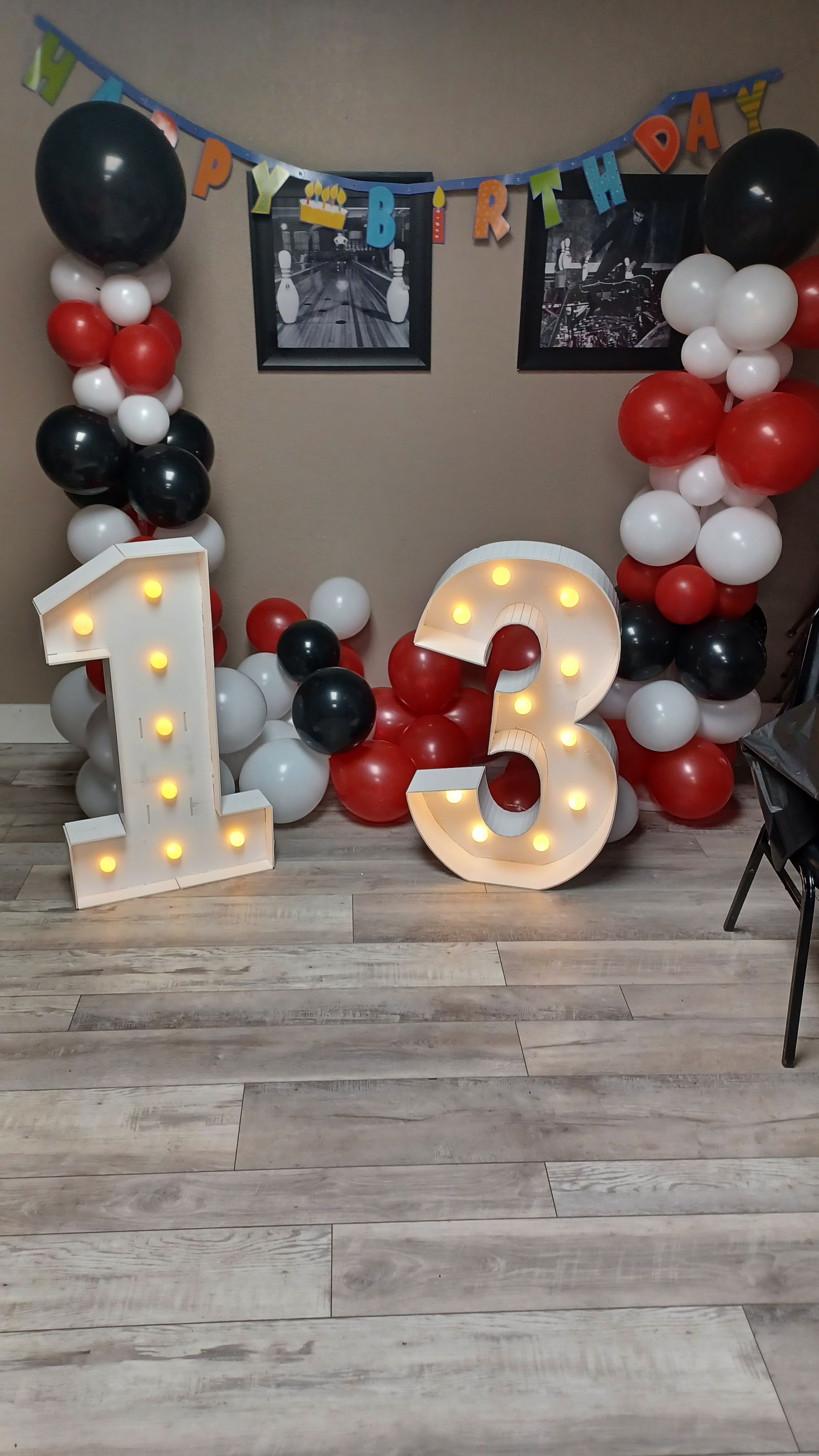 Birthday setup with illuminated number 13, red, white, and black balloon columns, and a chalkboard backdrop.