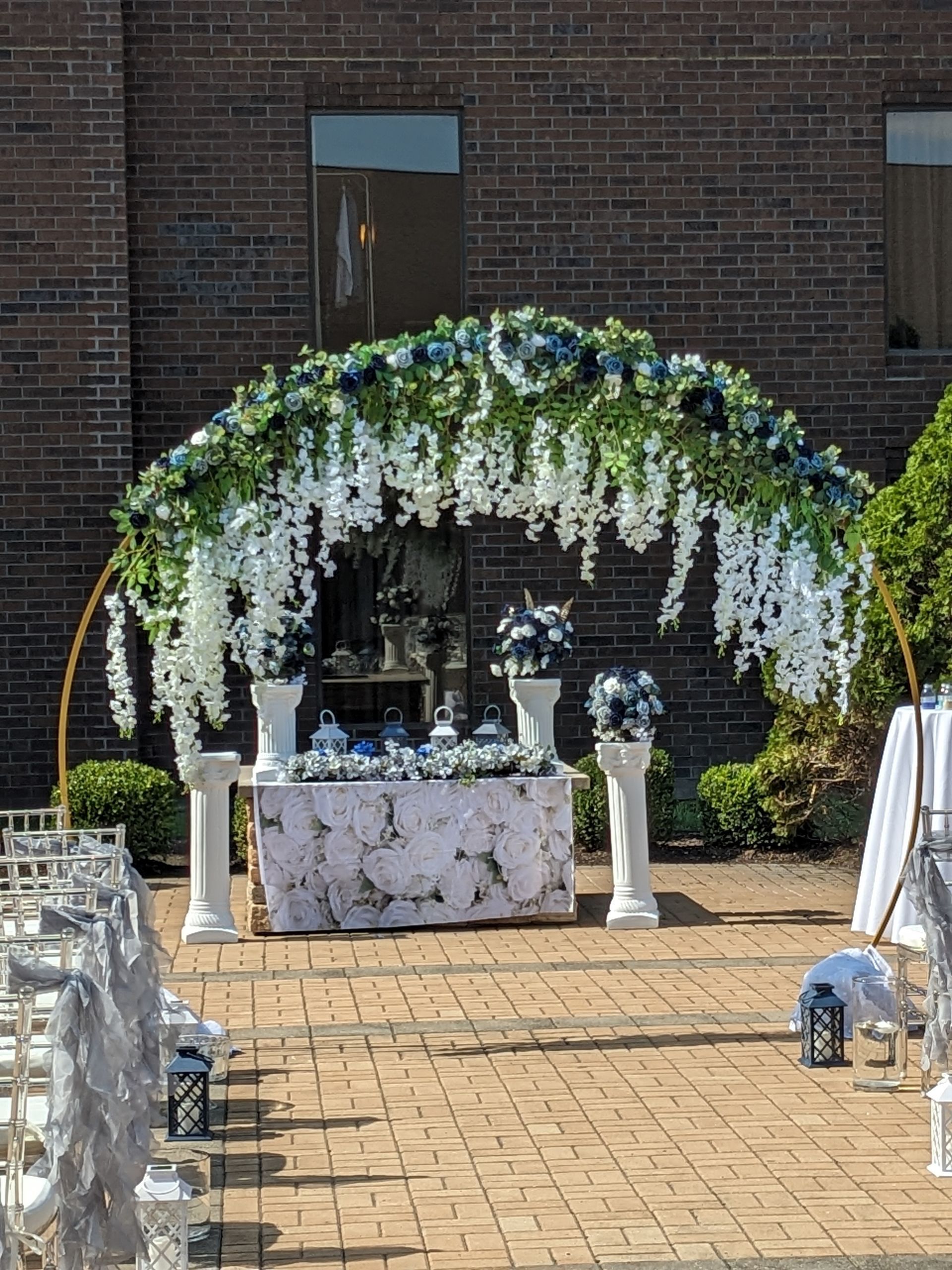 Floral archway with white drapes and a decorated table set up for an outdoor wedding ceremony