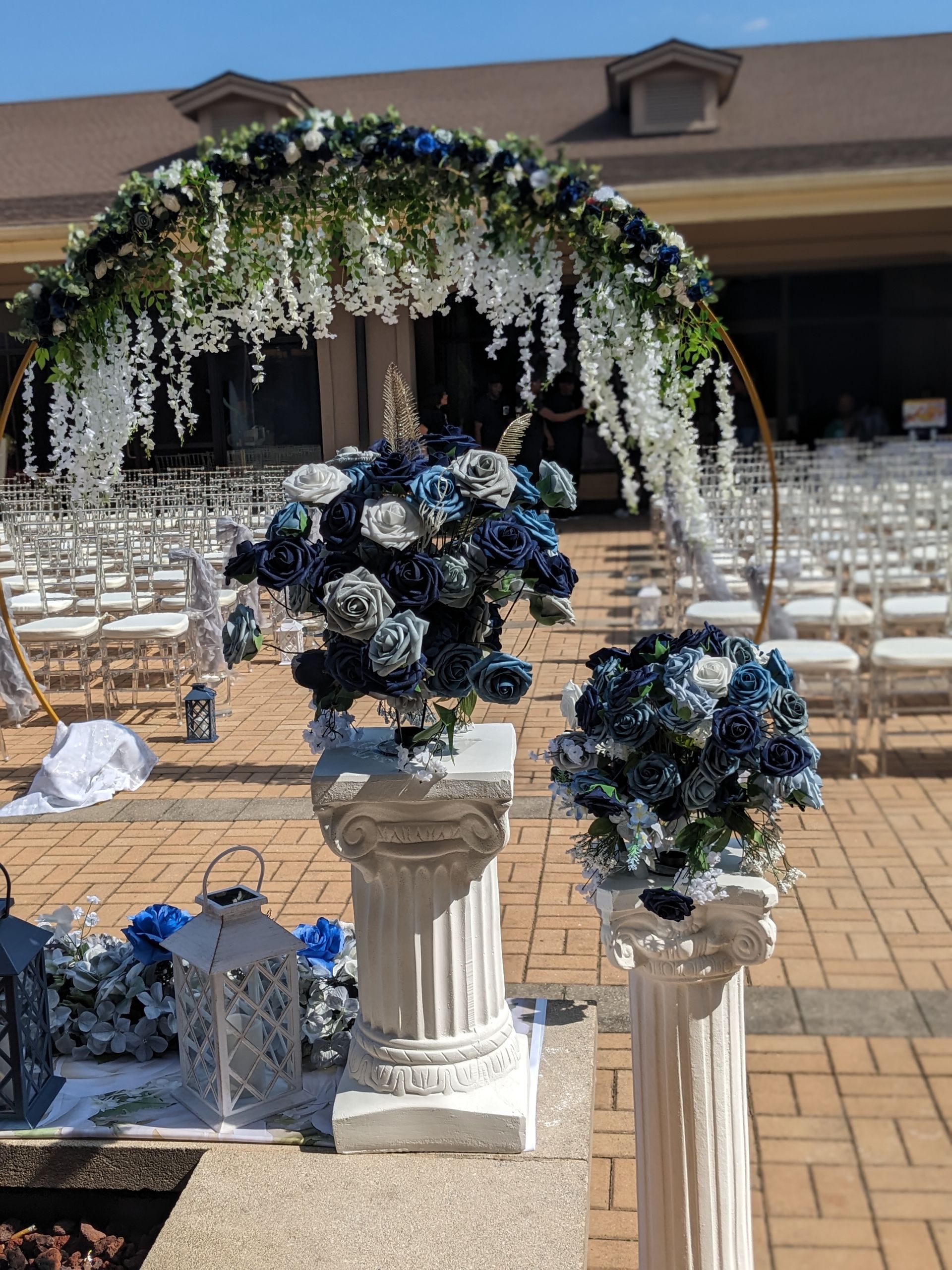 Floral arch and blue-white flower arrangements at an outdoor wedding ceremony setup