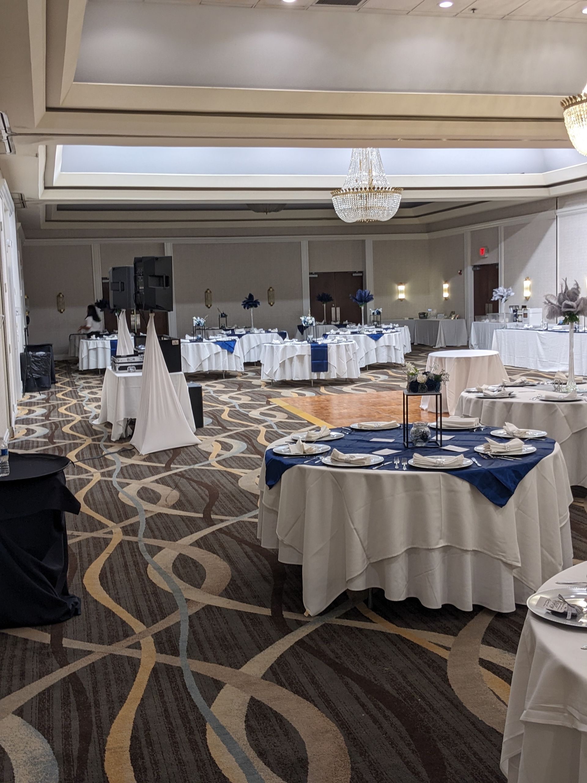 Banquet hall with round tables set for an event, blue tablecloths, chandeliers, and patterned carpet