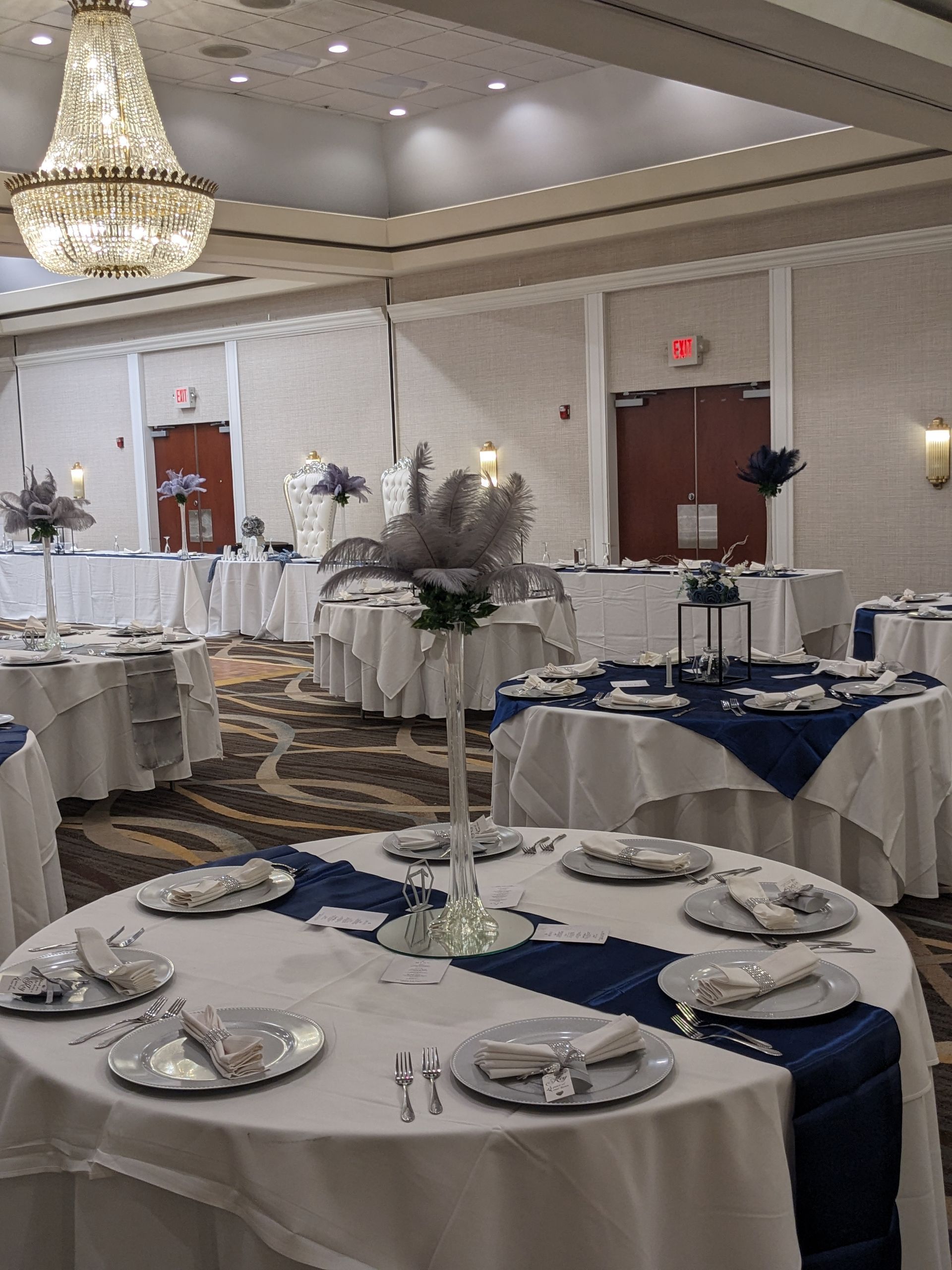 Elegant banquet hall with round tables, white chair covers, blue runners, and chandeliers