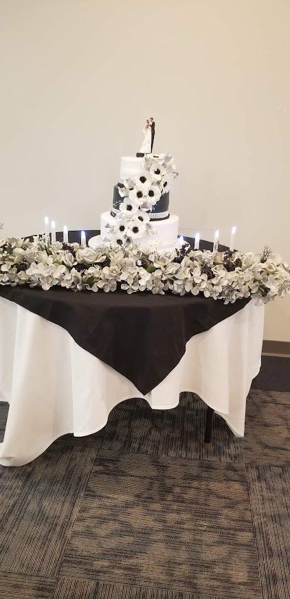 Black-and-white draped cake table with a tiered white cake and floral arrangement centerpiece