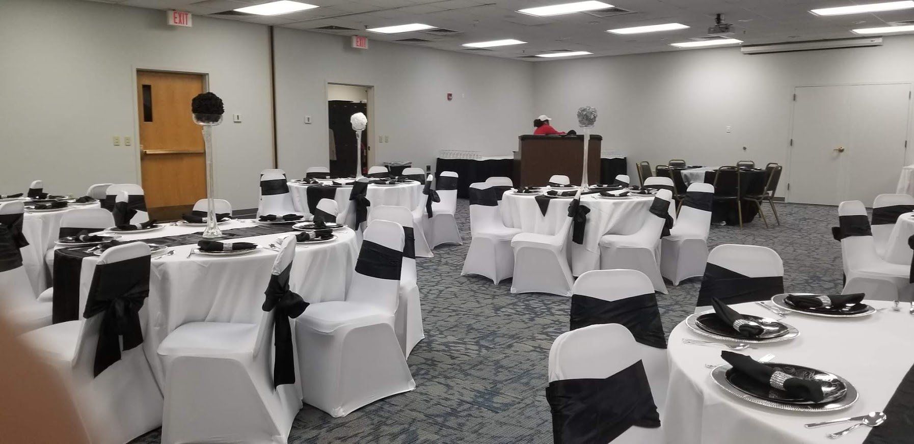 Conference room with round tables, white chair covers, and place settings set up for an event