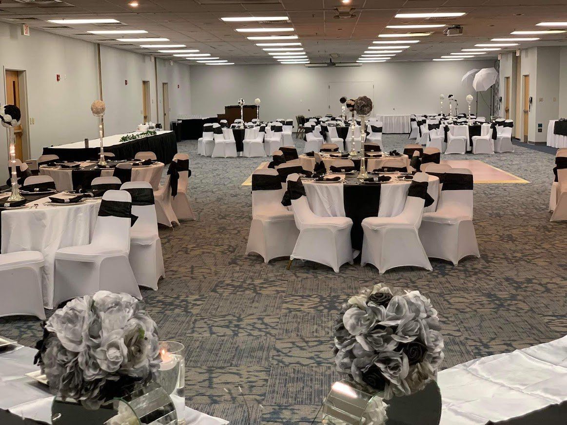 Banquet hall with round tables, white chair covers, and floral centerpieces under bright ceiling lights