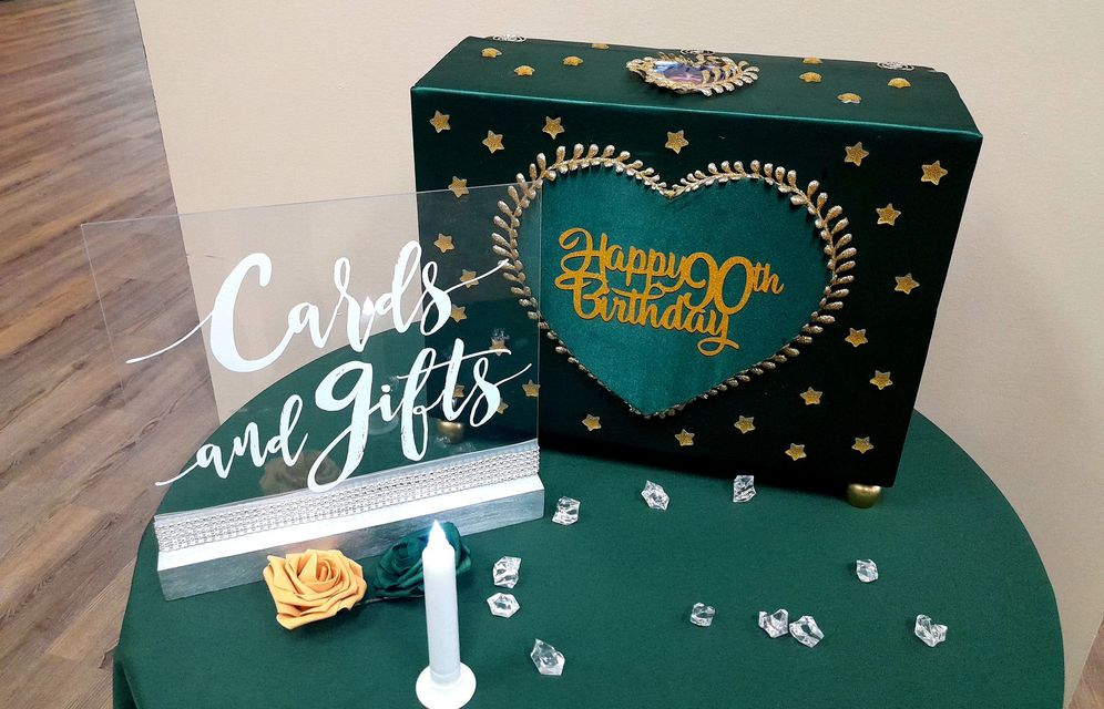 Green table display with a black-and-gold gift box, “Cards and Gifts” sign, and white floral decorations