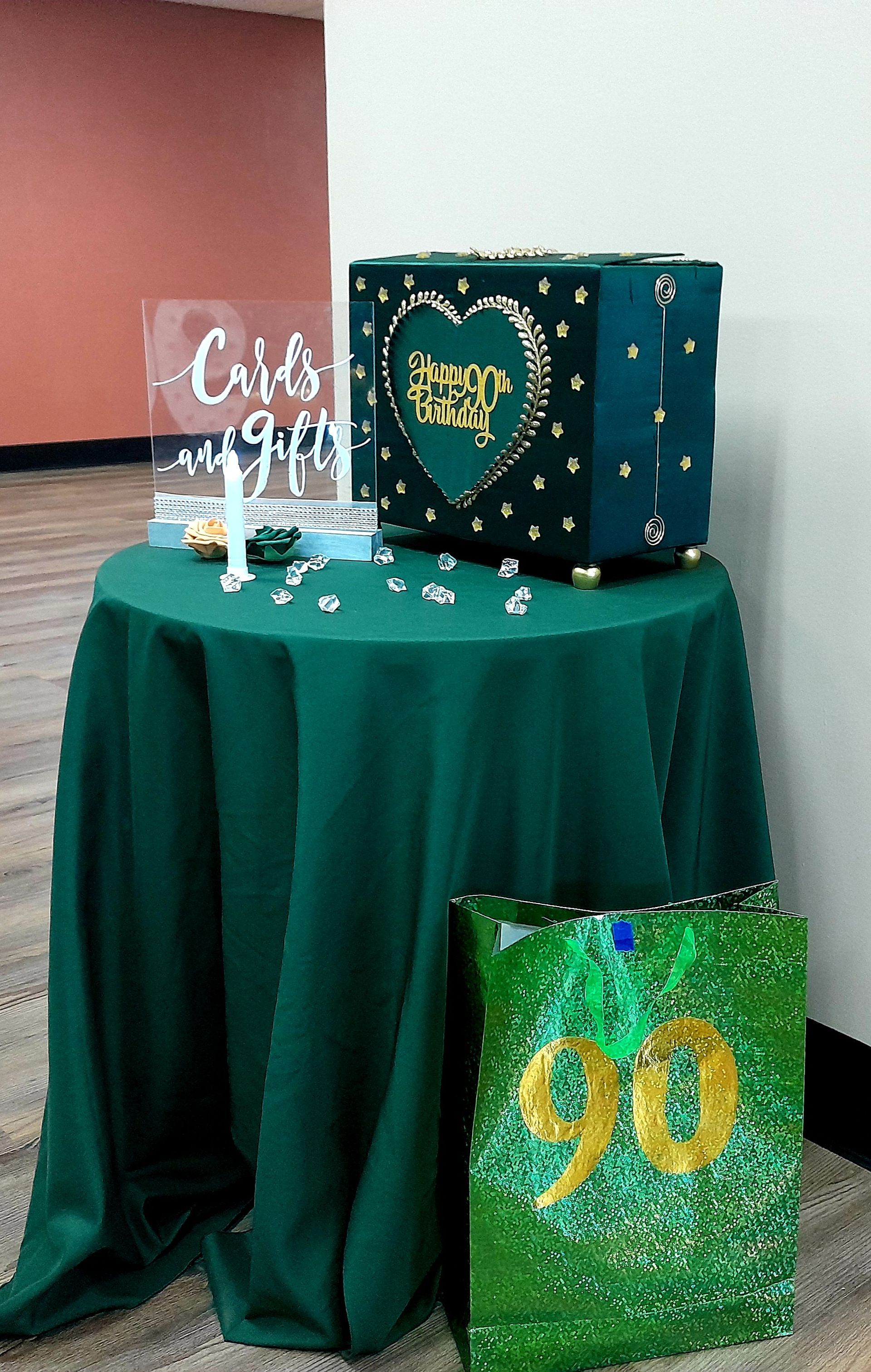 Decorated gift table with green tablecloth, heart display, and sparkling “90” sign for a celebration