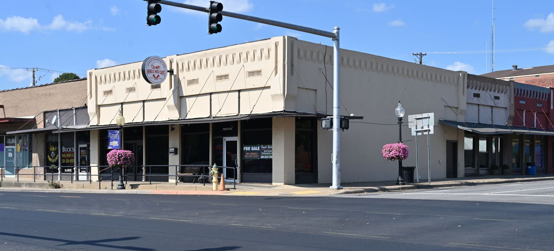 Corner storefront on a sunny street, with hanging flower baskets and traffic lights overhead modern day morrilton arkansas