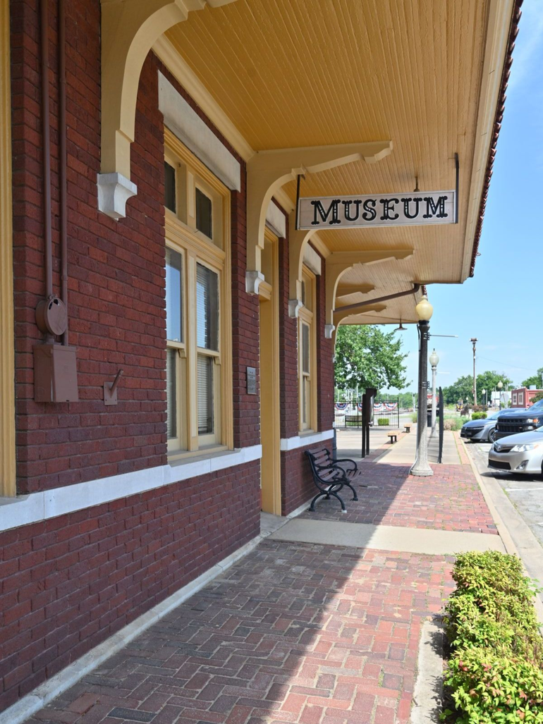 Brick museum building with arched windows, hanging sign, and bench | conway county arkansas