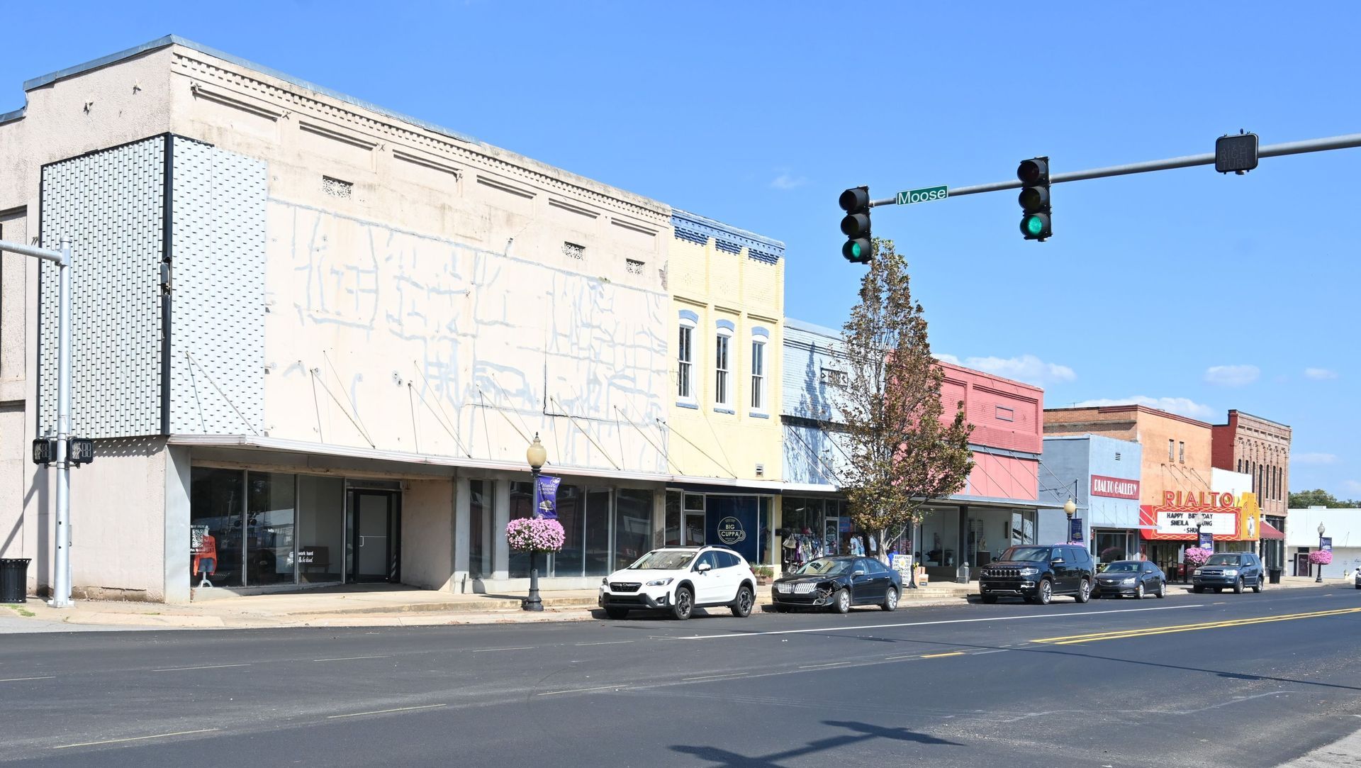 Modern-day Morrilton, AR, Downtown street with storefronts, parked cars, and traffic lights on a sunny day