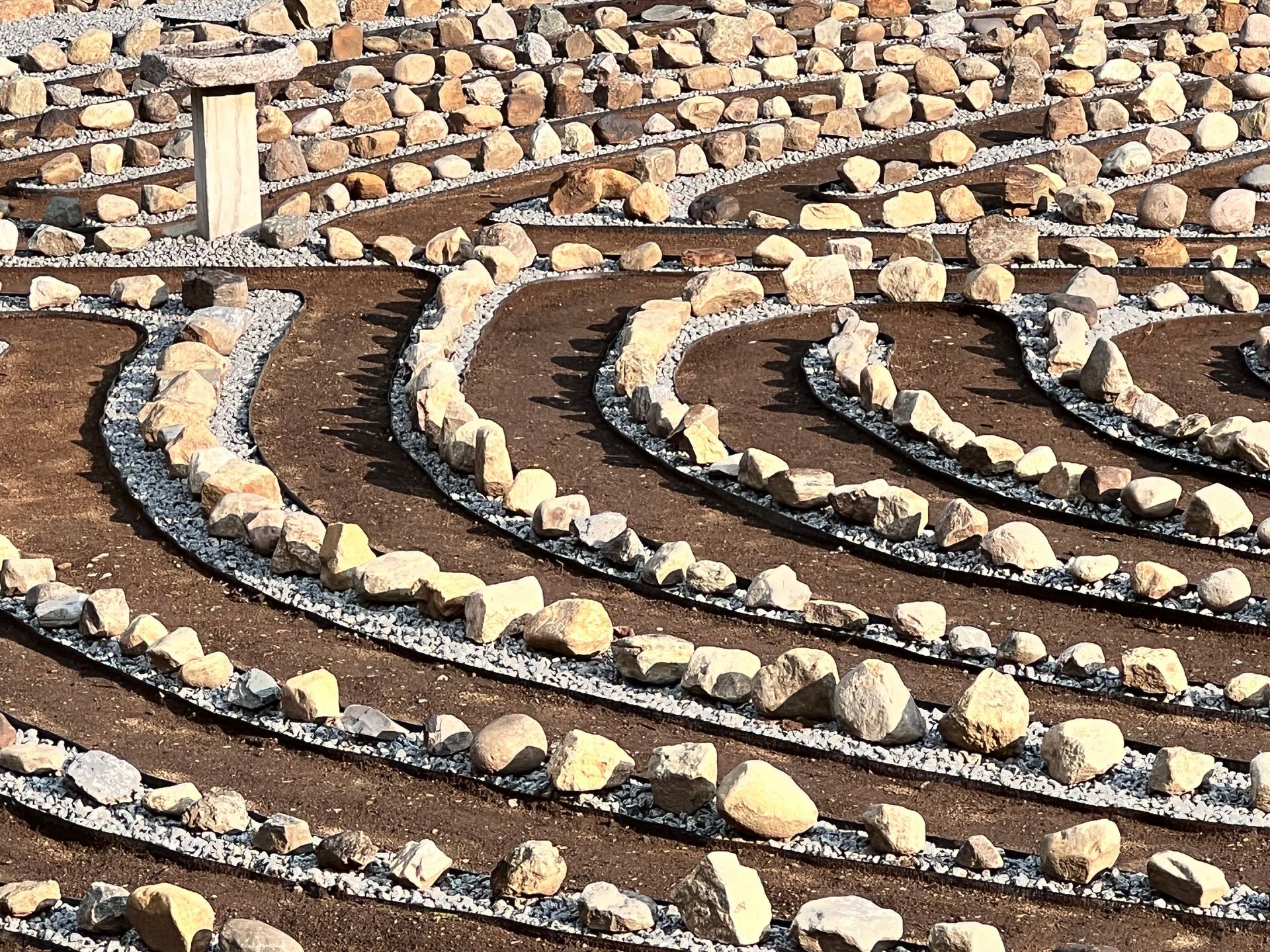 Image of labyrinth path with dirt walking portion and rocks sitting on stones in between the pathways. 