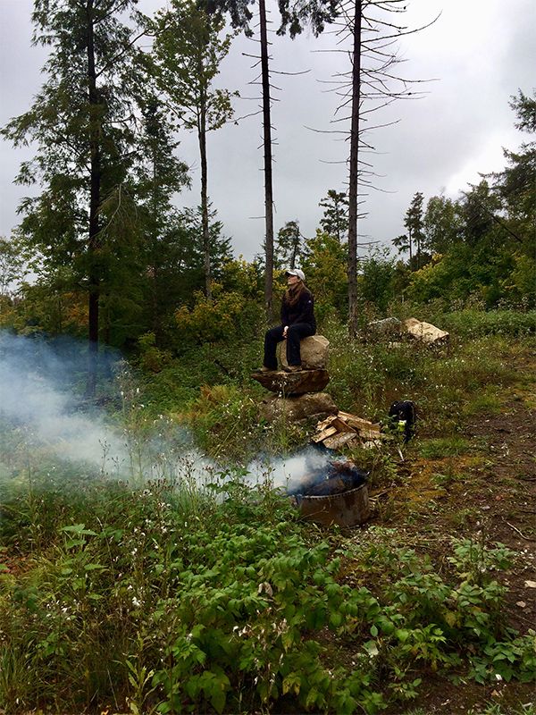 woman sitting on rocks looking into the distance near a camp fire
