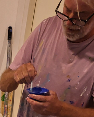 Jo Debije met een met verf bevlekt shirt mengt verf.