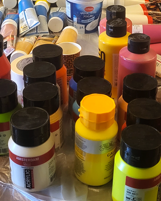 Een verzameling van diverse flesjes en tubes acrylverf in levendige kleuren, bij elkaar gegroepeerd op een oppervlak.