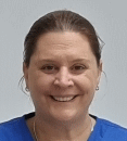 A woman in a blue scrub top is smiling for the camera.
