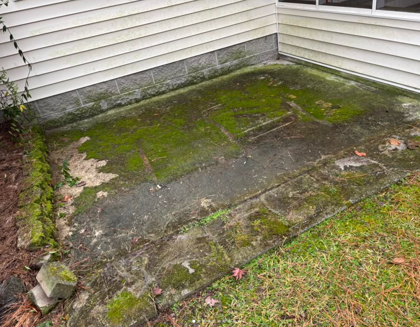 A dirty concrete patio with moss growing on it in front of a house.