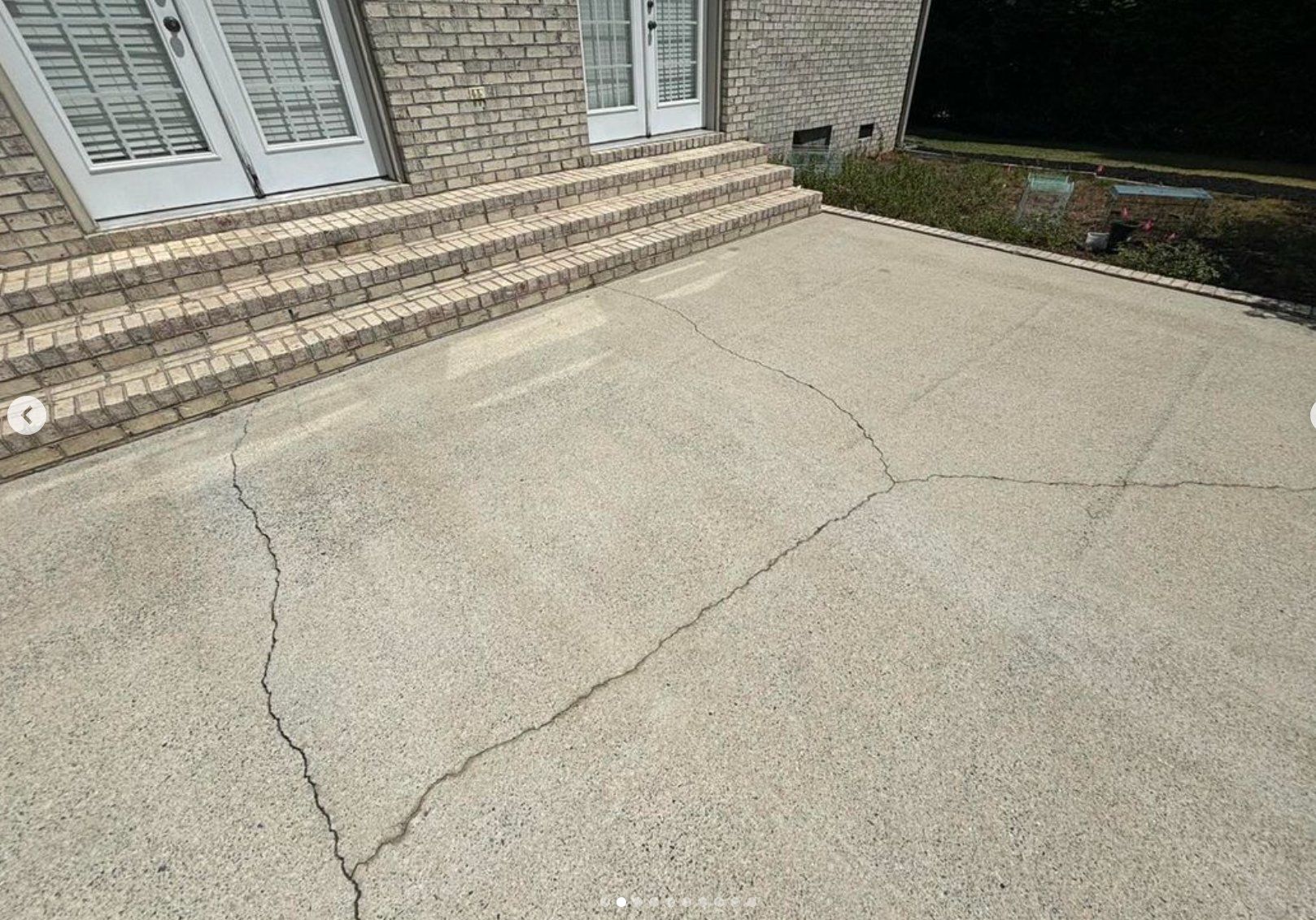 A cracked concrete patio in front of a brick house.