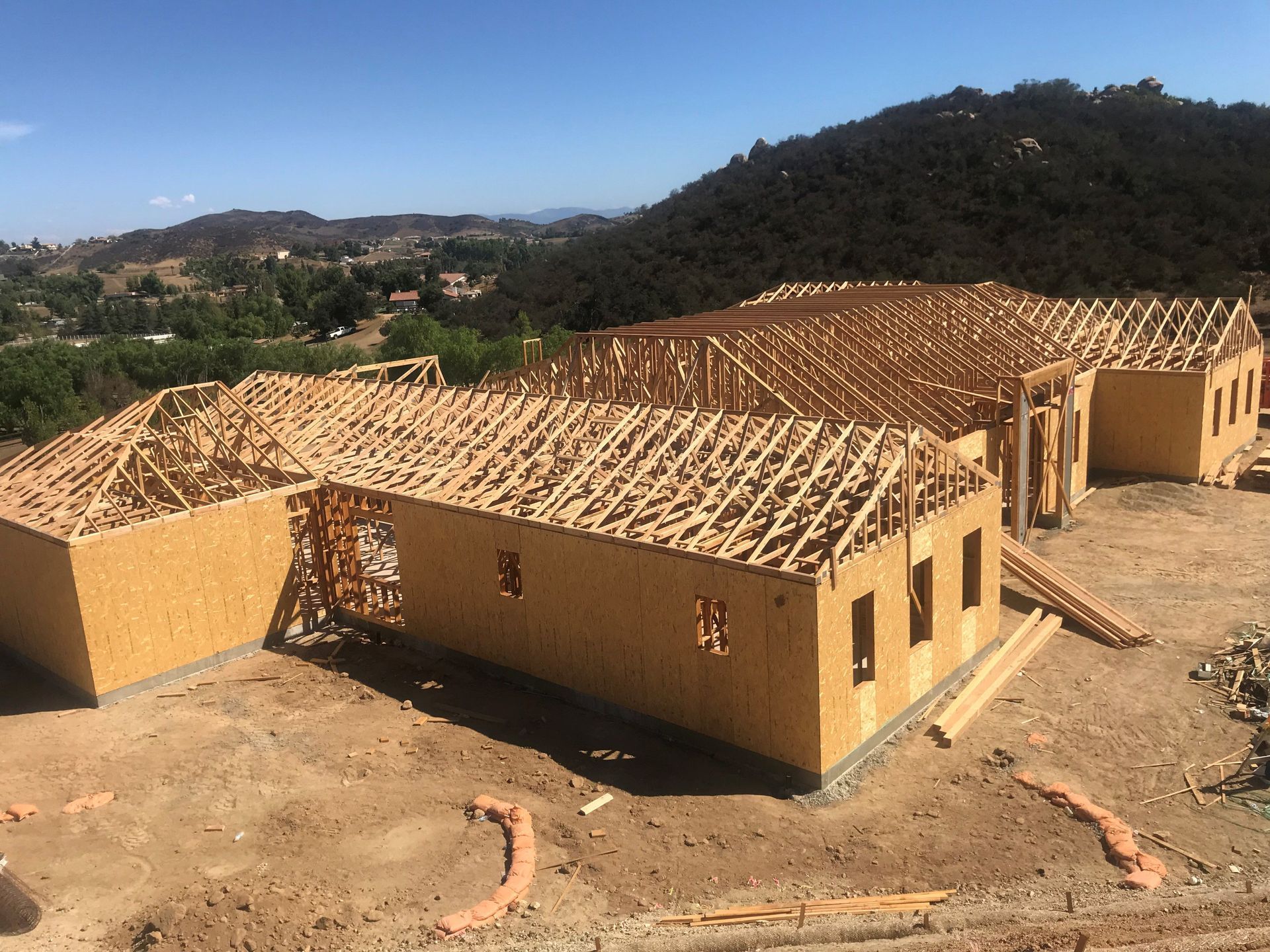Construction site: wood-framed house under construction; roof trusses in place, nestled in a hilly landscape.