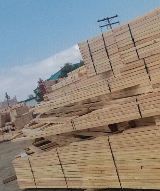 Stacks of lumber, likely at a lumberyard, under a blue sky.
