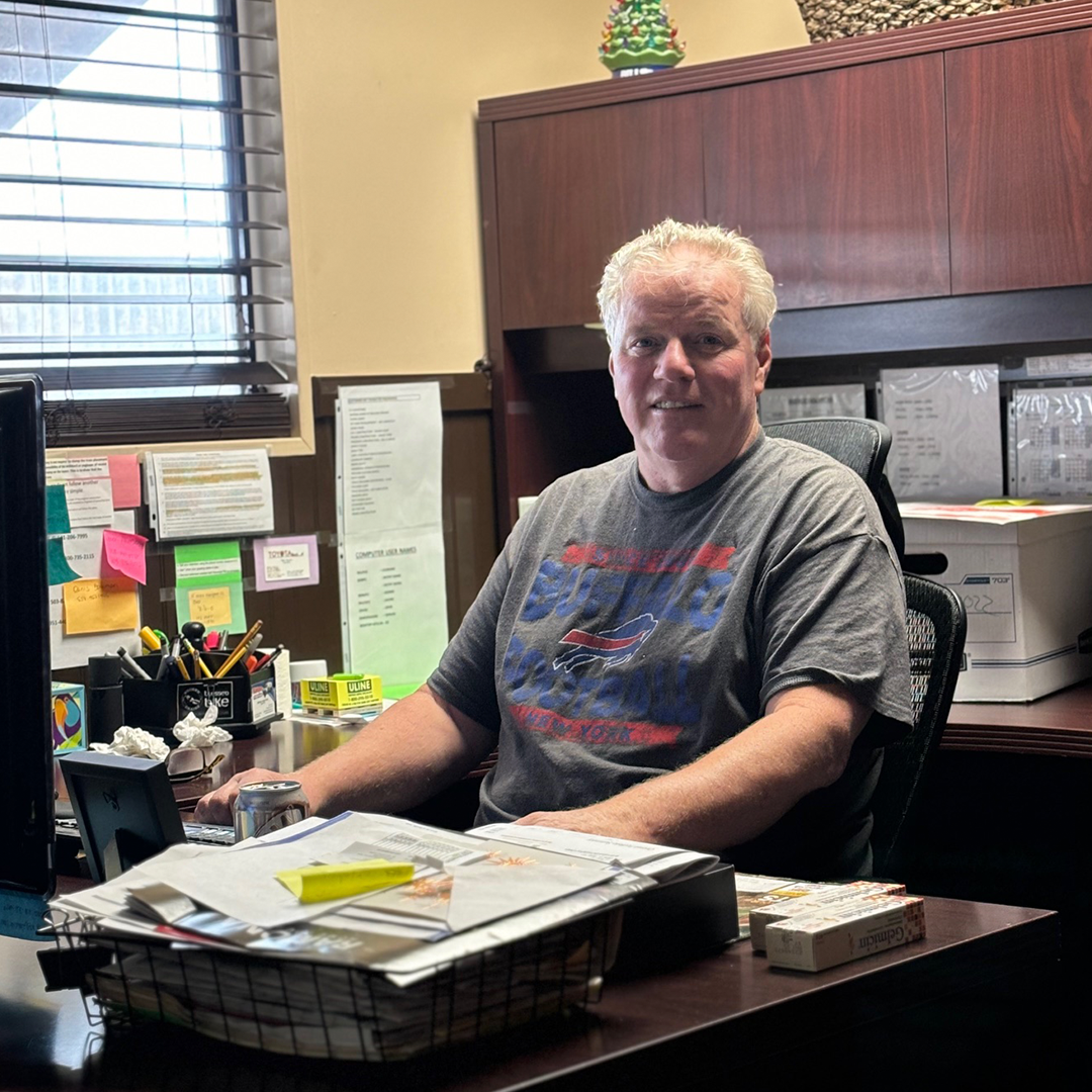 Man sitting at desk, grey t-shirt, working in office with documents.