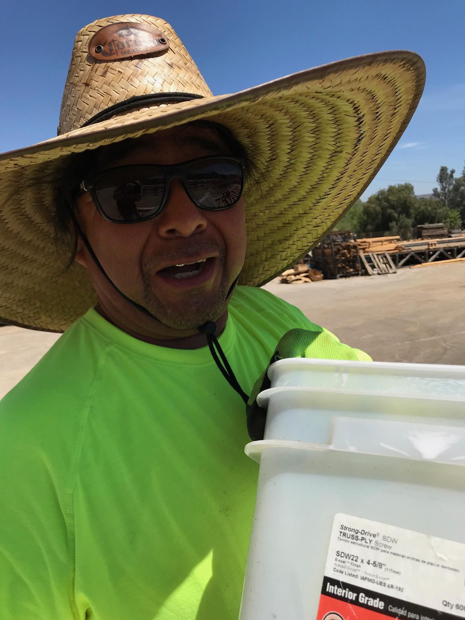 Man in straw hat and sunglasses smiles while holding a white bucket outdoors.