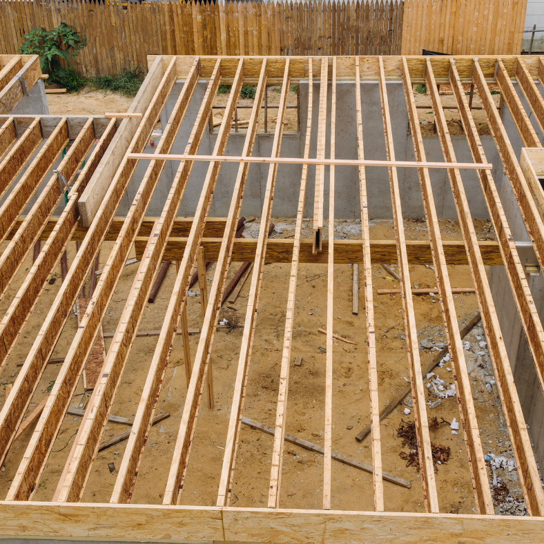 Wooden house frame under construction, with beams and open space.