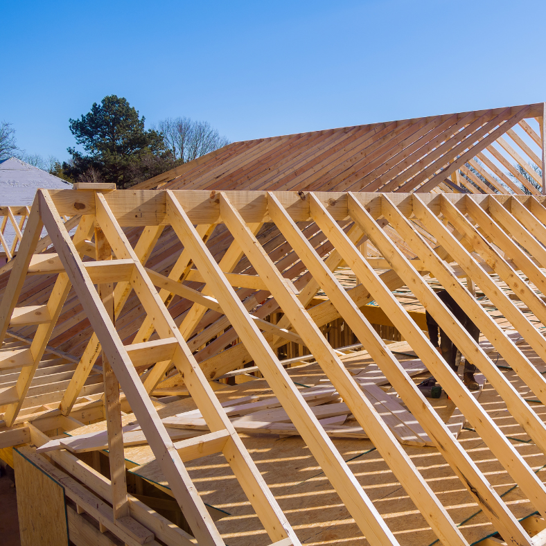 Wooden roof frame under construction against a clear blue sky.