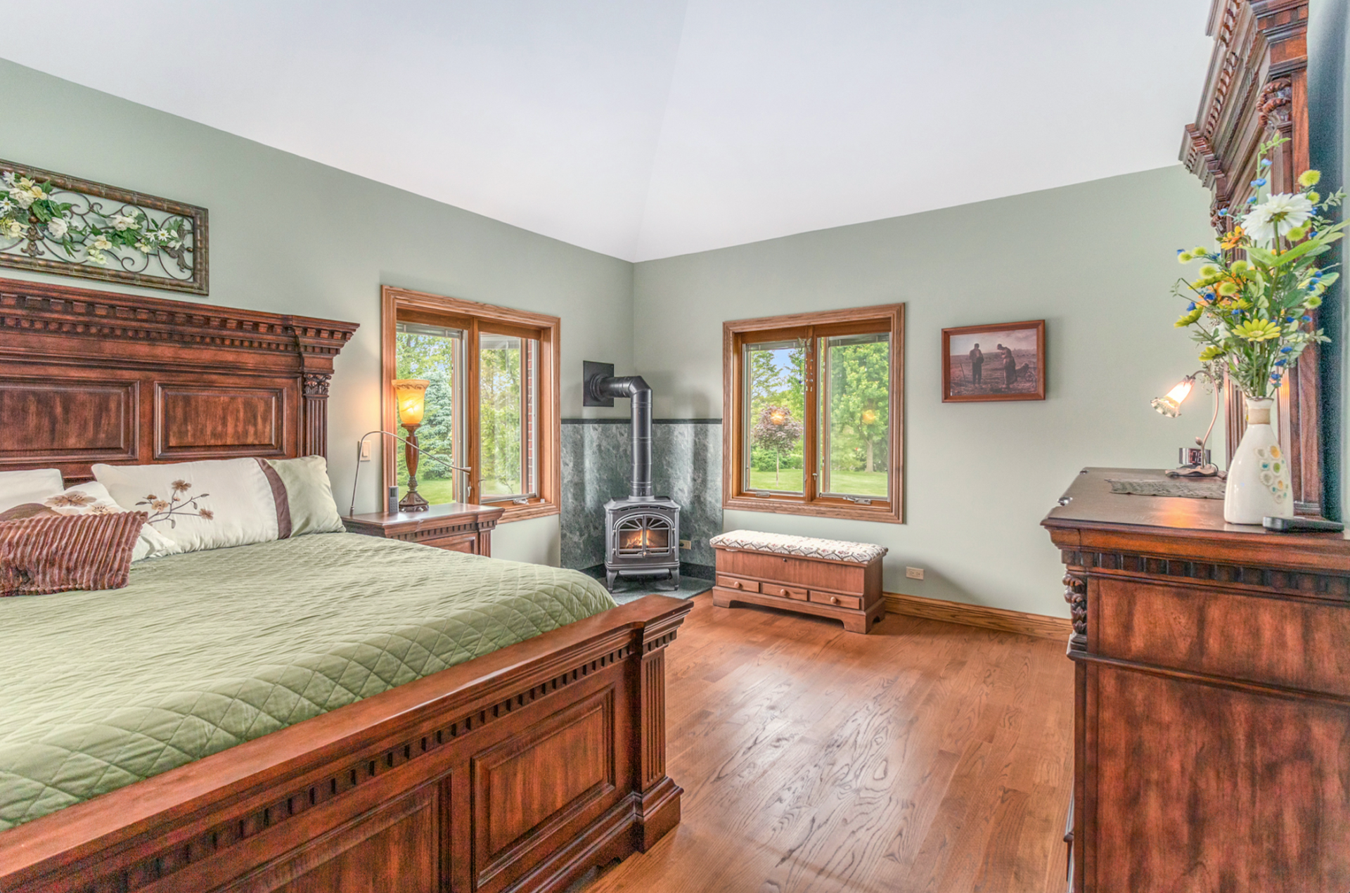A bedroom with a king size bed , dresser , mirror and fireplace.