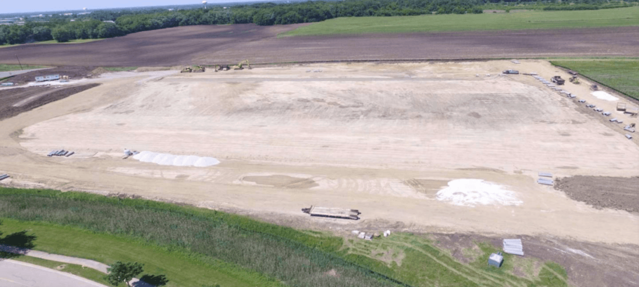An aerial view of a large dirt field surrounded by trees.